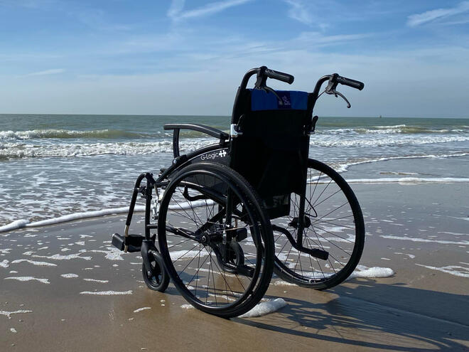 A picture of an empty wheelchair on the shoreline, with the waves washing up around the wheels